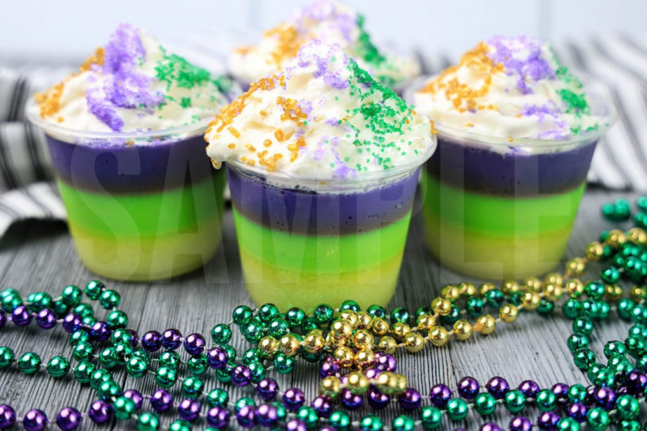 The Mardi Gras Layered Jello Shots comes in a clear jello shot cup with a white striped napkin on a gray wood backdrop.