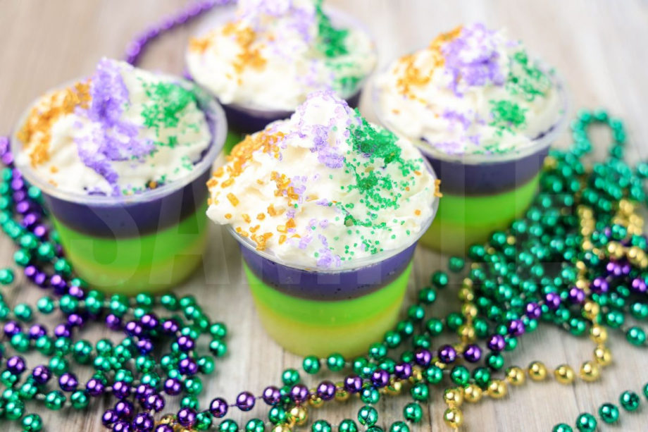 The Mardi Gras Layered Jello Shots comes in a clear jello shot cup with a denim napkin on a rustic wood backdrop.