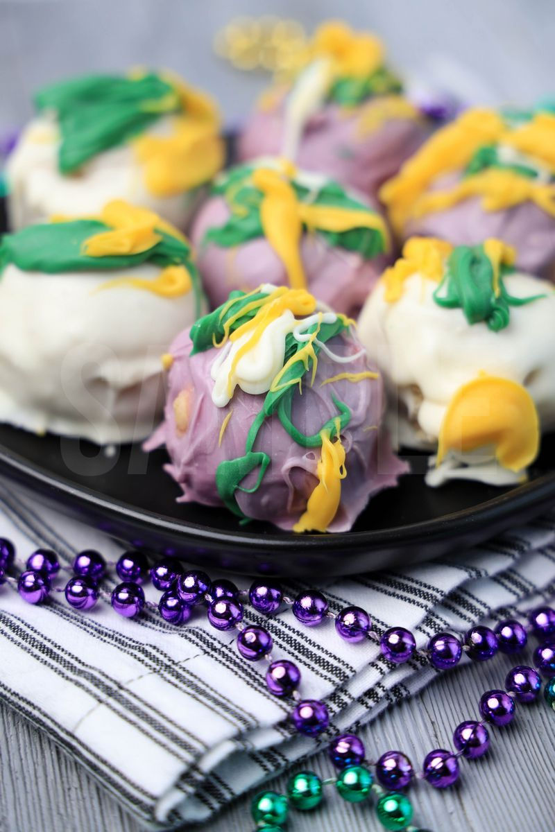 The Mardi Gras Oreo Balls comes on a black plate with white striped napkin on a gray wood backdrop.