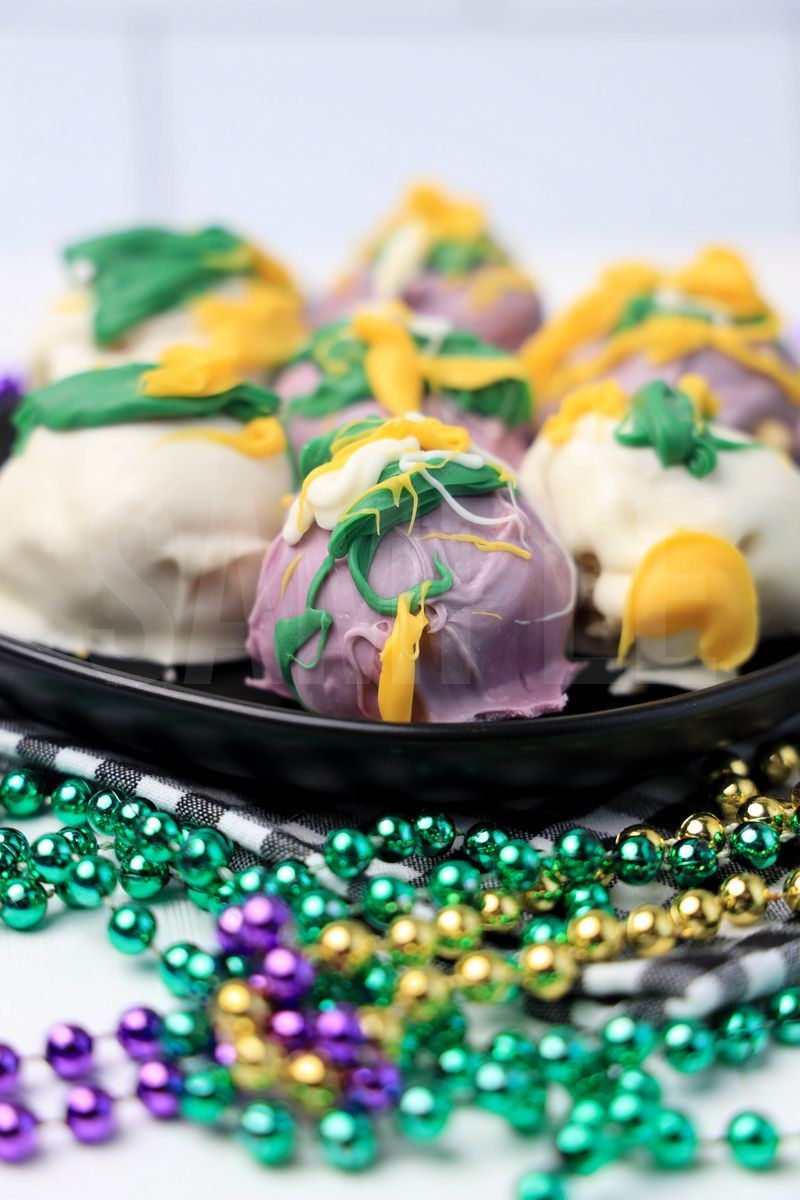 The Mardi Gras Oreo Balls comes on a black plate with a plaid napkin on a white wood backdrop.