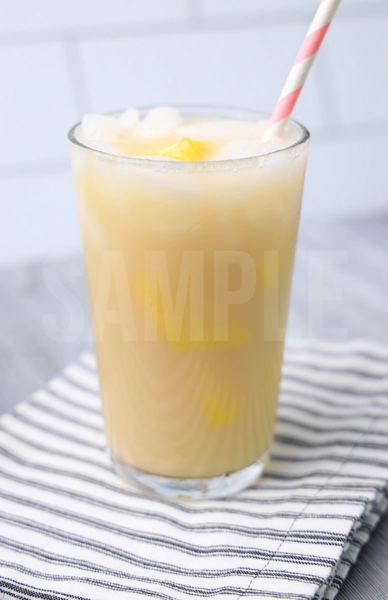 The Paradise Drink comes in a clear glass with a white striped napkin on a gray wood backdrop.