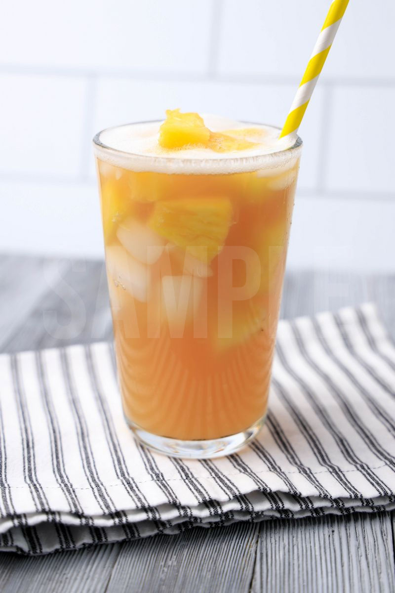 The Pineapple Passionfruit Refresher comes in a clear glass with a white striped napkin on a gray wood backdrop.