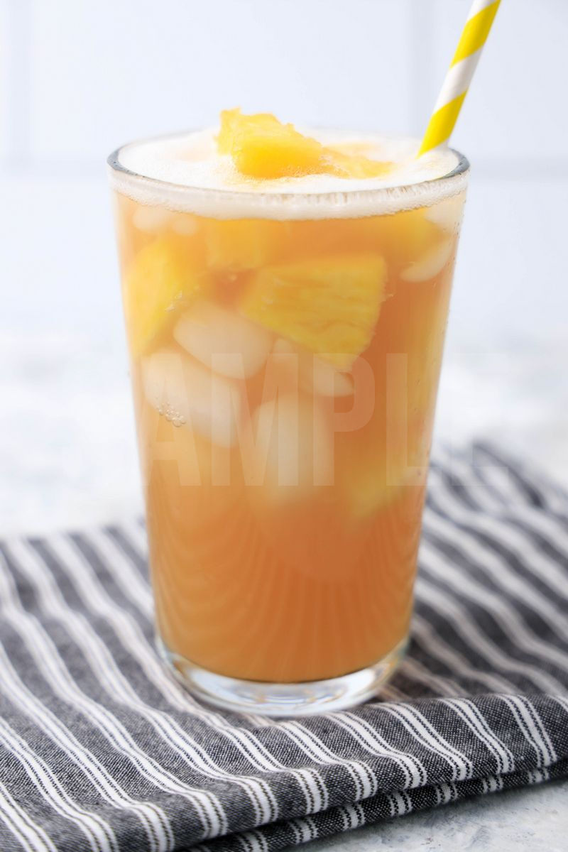 The Pineapple Passionfruit Refresher comes in a clear glass with a gray striped napkin on a marble backdrop.