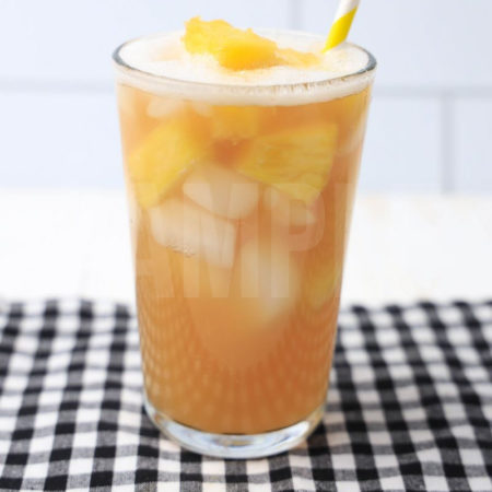 The Pineapple Passionfruit Refresher comes in a clear glass with a plaid napkin on a white wood backdrop.