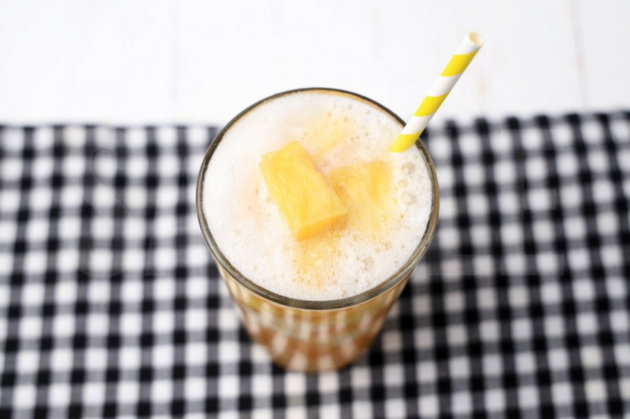 The Pineapple Passionfruit Refresher comes in a clear glass with a plaid napkin on a white wood backdrop.