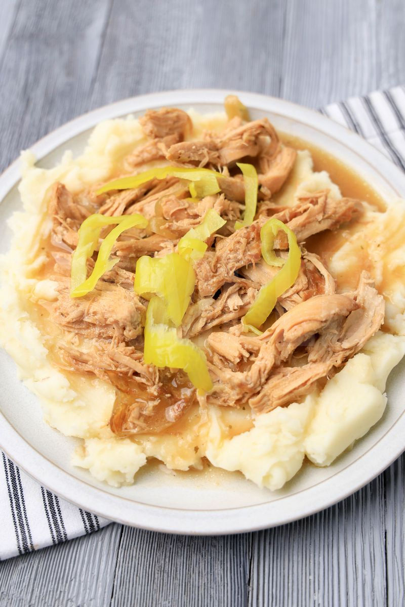 The Slow Cooker Mississippi Chicken comes on a stone plate with a white striped napkin on a gray wood backdrop.
