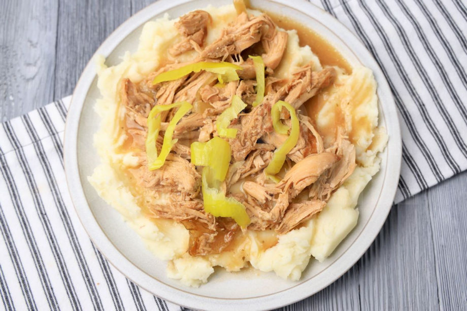 The Slow Cooker Mississippi Chicken comes on a stone plate with a white striped napkin on a gray wood backdrop.