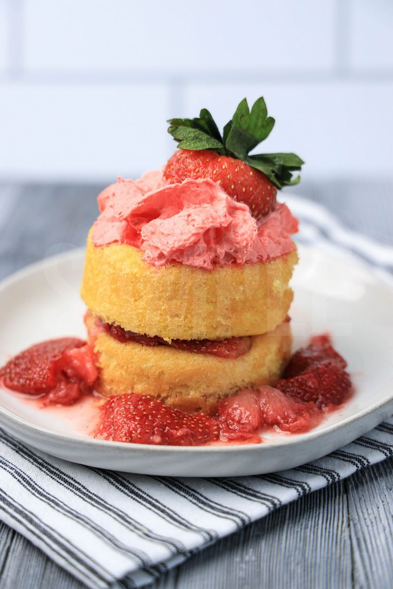The Strawberry Shortcake comes on a white plate with a white striped napkin on a gray wood backdrop.
