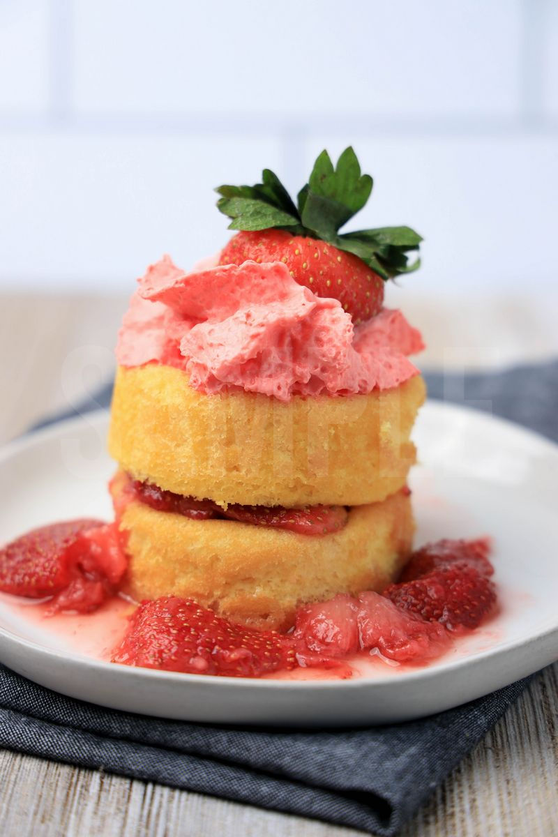 The Strawberry Shortcake comes on a white plate with a denim napkin on a rustic wood backdrop.