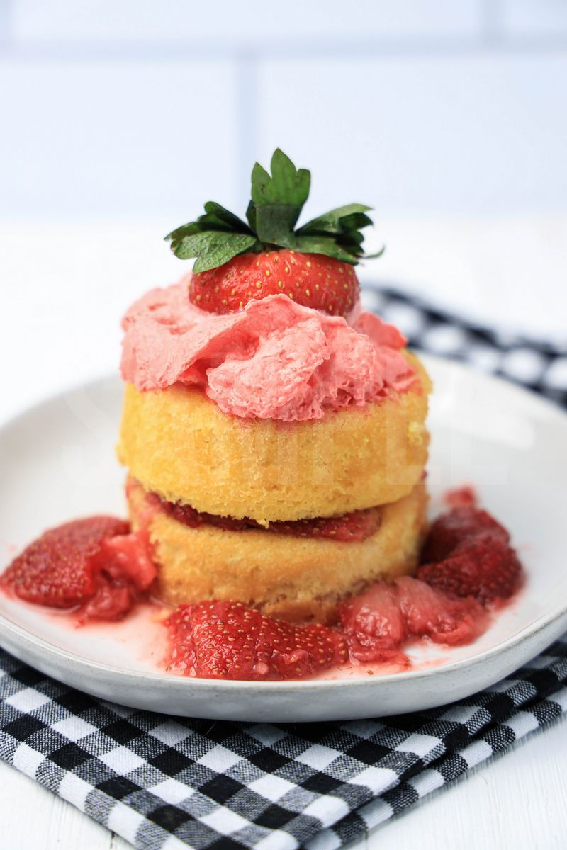 The Strawberry Shortcake comes on a white plate with a plaid napkin on a white wood backdrop.
