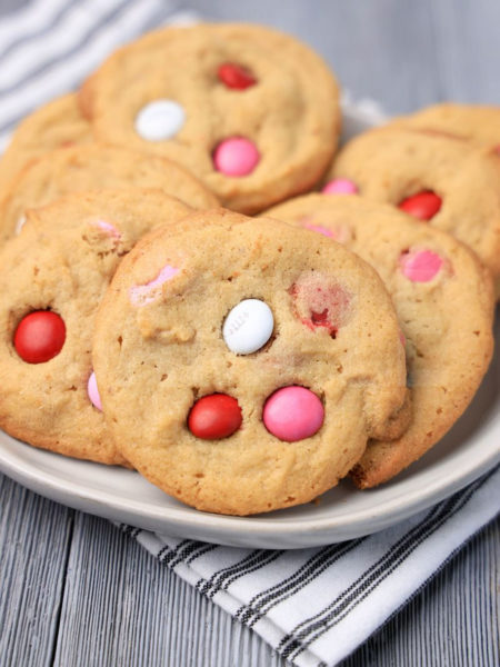 The Valentine's M&M Cookies comes on a white plate with a white striped napkin on a gray wood backdrop.