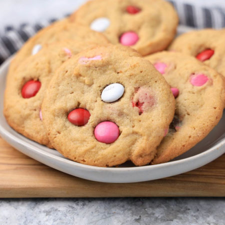 The Valentine's M&M Cookies comes on a white plate with a gray striped napkin on a marble backdrop.