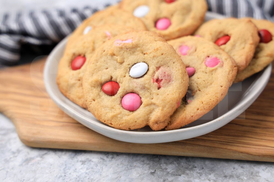 The Valentine's M&M Cookies comes on a white plate with a gray striped napkin on a marble backdrop.