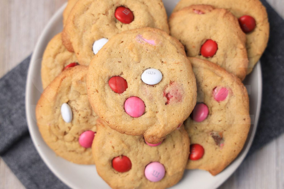 The Valentine's M&M Cookies comes on a white plate with a denim napkin on a rustic wood backdrop.