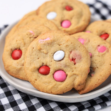 The Valentine's M&M Cookies comes on a white plate with a plaid napkin on a white wood backdrop.