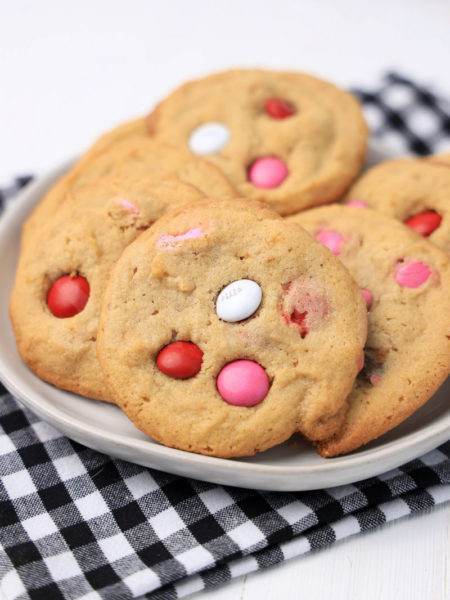 The Valentine's M&M Cookies comes on a white plate with a plaid napkin on a white wood backdrop.