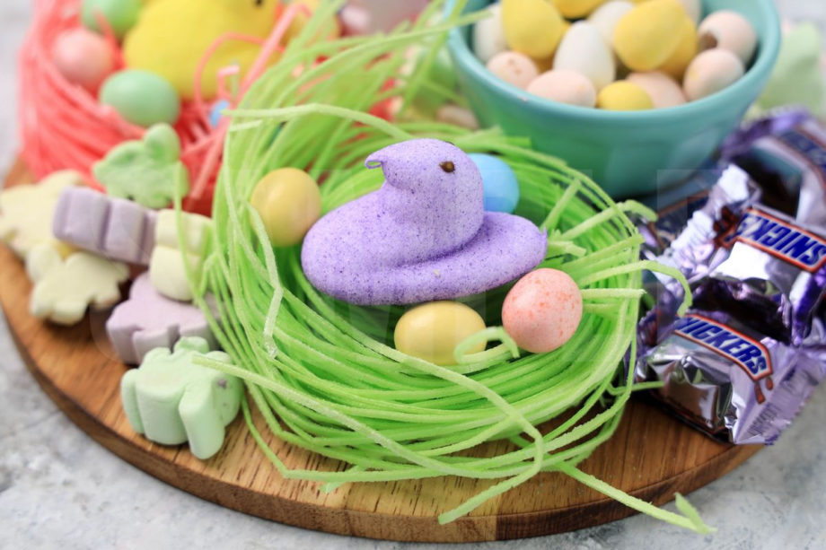 The Easter Candy Charcuterie Board comes on a wood egg board on a marble backdrop.