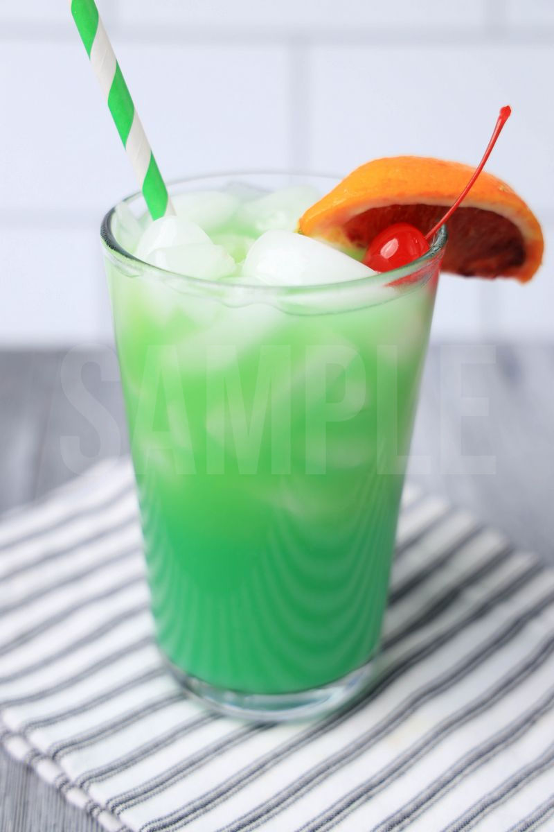 The Green Drunken Leprechaun comes in a clear glass with a white striped napkin on a gray wood backdrop.