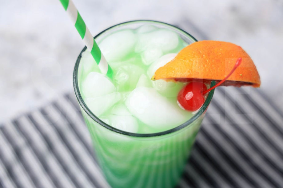 The Green Drunken Leprechaun comes in a clear glass with a gray striped napkin on a marble backdrop.