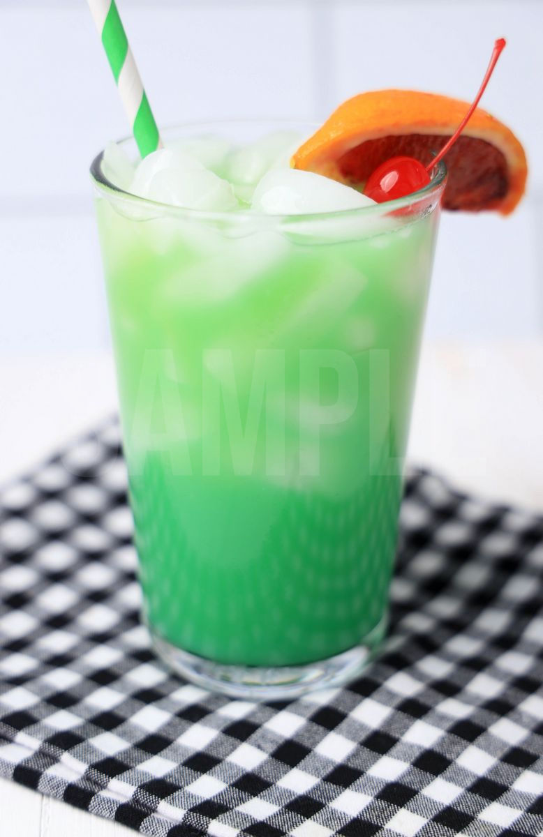 The Green Drunken Leprechaun comes in a clear glass with a plaid napkin on a white wood backdrop.