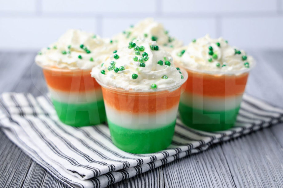The Irish Flag Jello Shots come in a clear plastic cup with a white striped napkin on a gray wood backdrop.