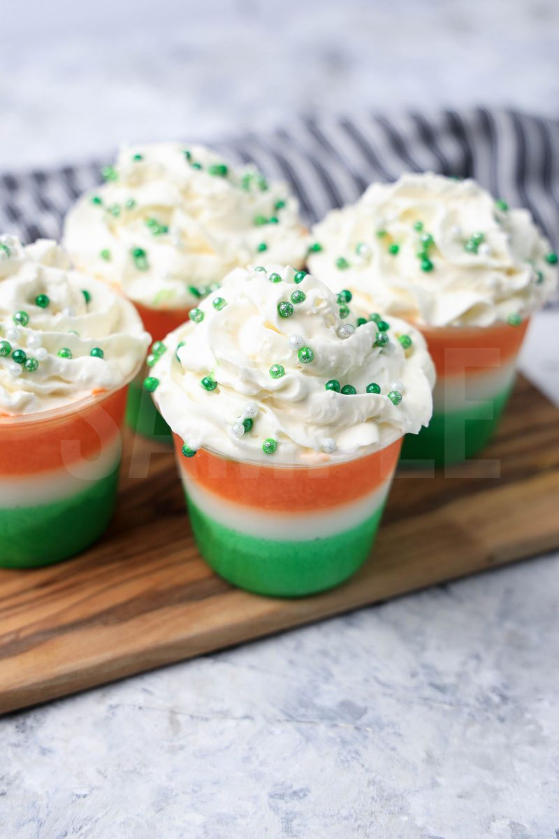 The Irish Flag Jello Shots come in a clear plastic cup with a gray striped napkin on a marble backdrop.