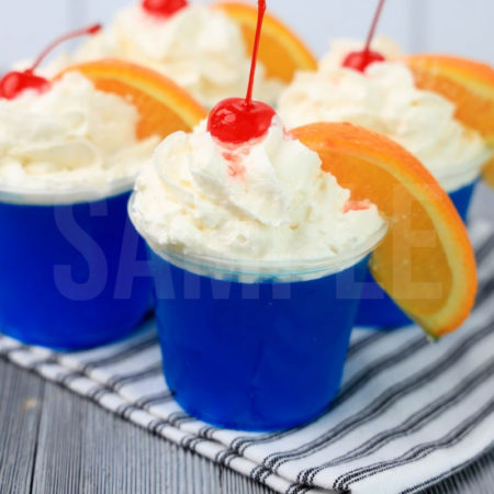 The Ocean Water Jello Shots comes in clear cups on a white striped napkin with a gray wood backdrop.