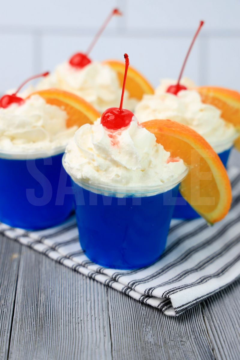 The Ocean Water Jello Shots comes in clear cups on a white striped napkin with a gray wood backdrop.