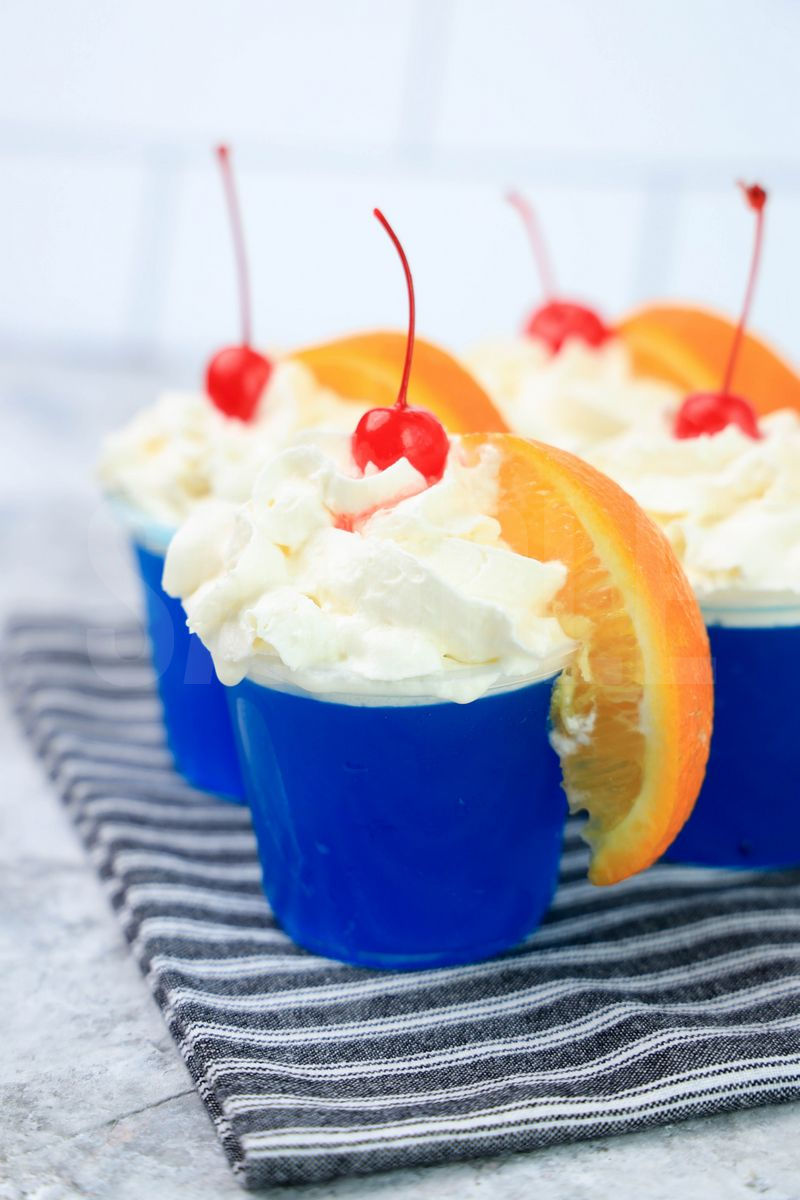 The Ocean Water Jello Shots comes in clear cups on a gray striped napkin with a marble backdrop.