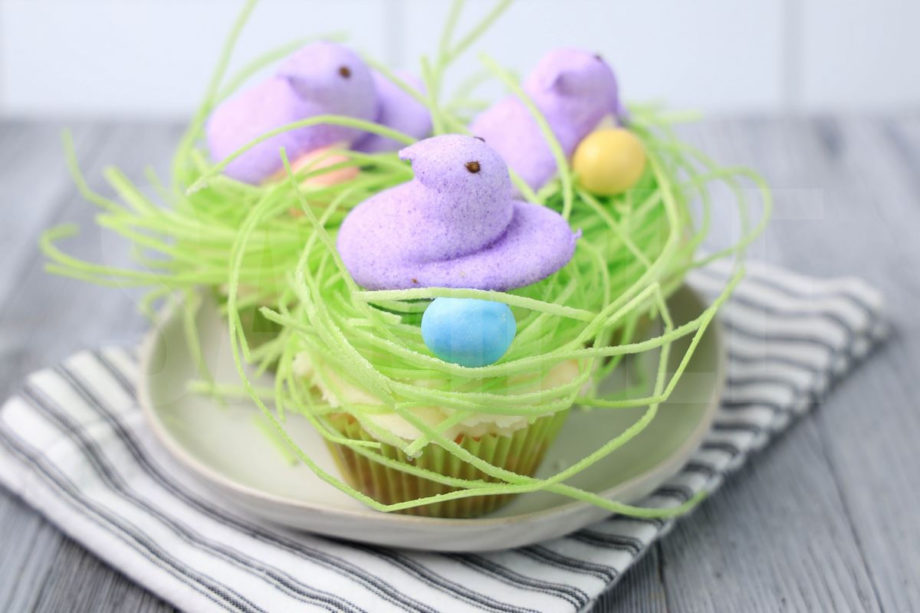 Peeps Bird Nest Cupcakes comes on a white plate on a white striped napkin with a gray wood backdrop.