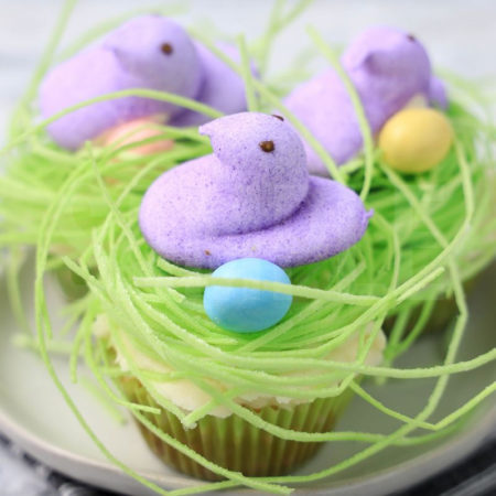 The Peeps Bird Nest Cupcakes comes on a white plate on a gray striped napkin with a marble backdrop.