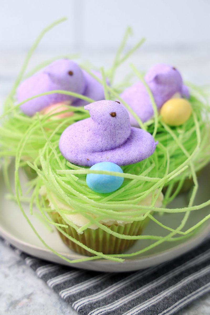 The Peeps Bird Nest Cupcakes comes on a white plate on a gray striped napkin with a marble backdrop.