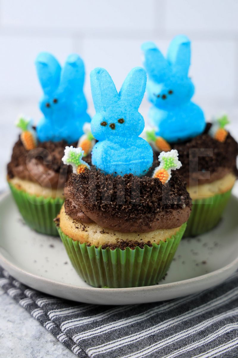 The Peeps Bunny Dirt Cupcakes comes on a white plate on a gray striped napkin with a marble backdrop.