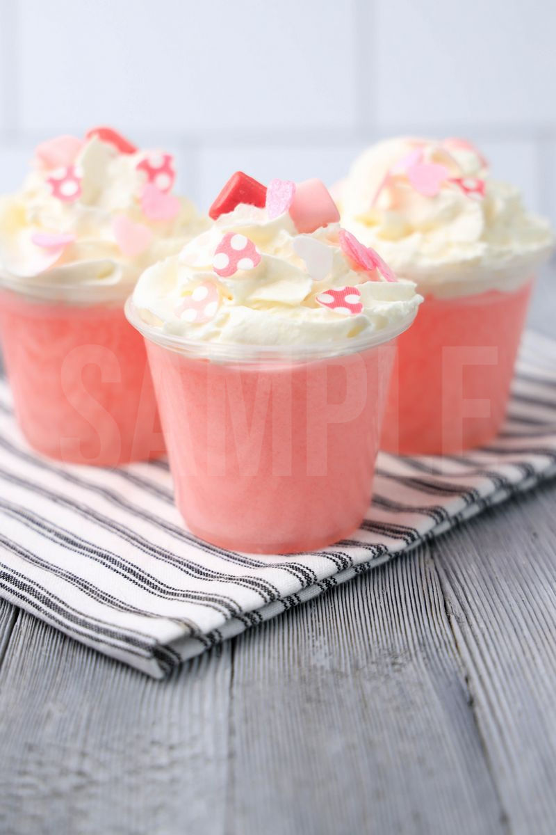 The Pink Starburst Jello Shots comes in clear cups on a gray striped napkin with a gray wood backdrop.