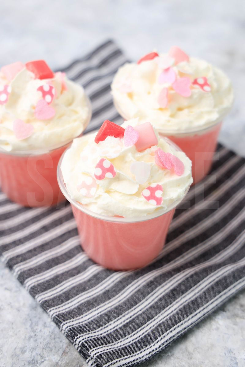 The Pink Starburst Jello Shots comes in clear cups on a white striped napkin with a marble backdrop.