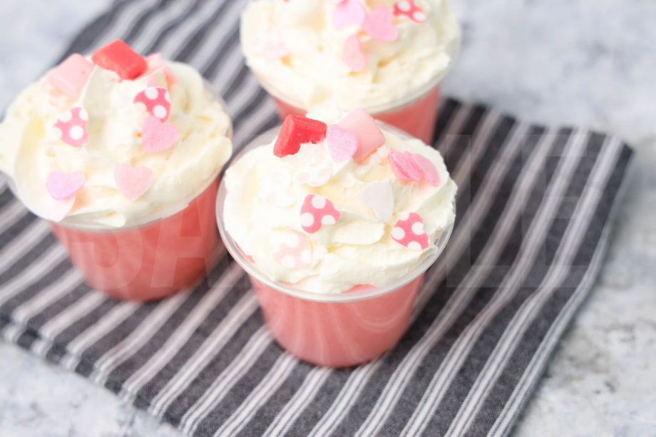 The Pink Starburst Jello Shots comes in clear cups on a white striped napkin with a marble backdrop.