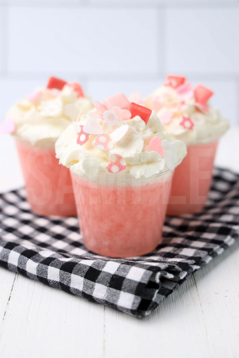 The Pink Starburst Jello Shots comes in clear cups on a plaid napkin with a white wood backdrop.