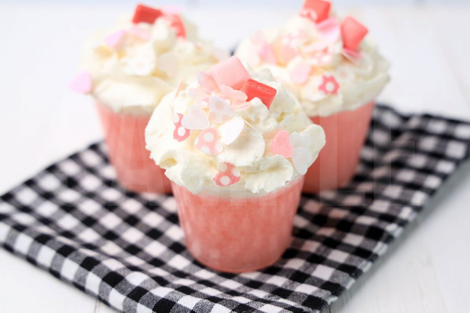 The Pink Starburst Jello Shots comes in clear cups on a plaid napkin with a white wood backdrop.