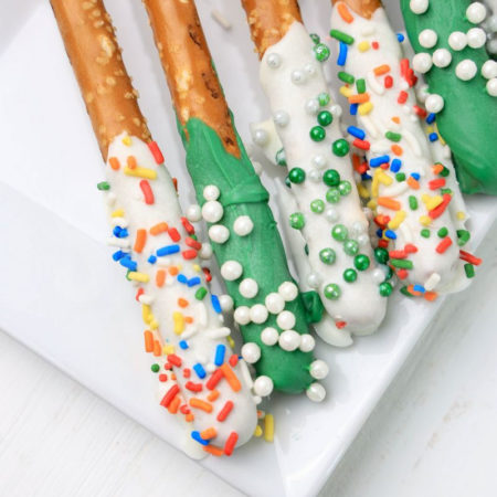 The St. Patrick's Pretzel Rods comes on a white plate on a plaid napkin with a white wood backdrop.