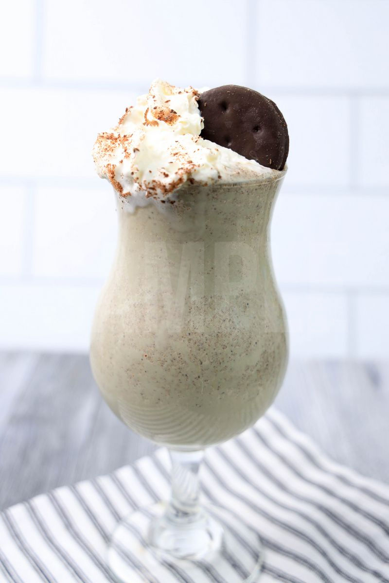Thin Mint Shake comes in a clear glass with a white striped napkin on a gray wood backdrop.