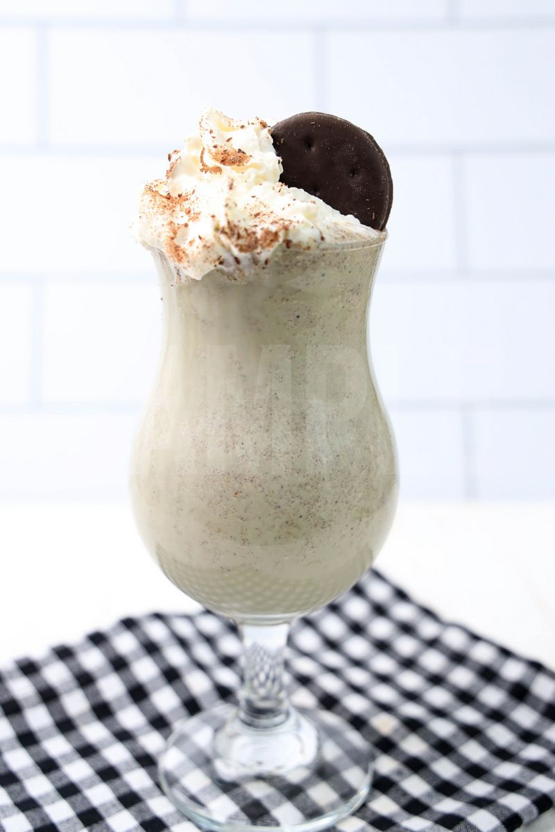 Thin Mint Shake comes in a clear glass with a plaid napkin on a white wood backdrop.