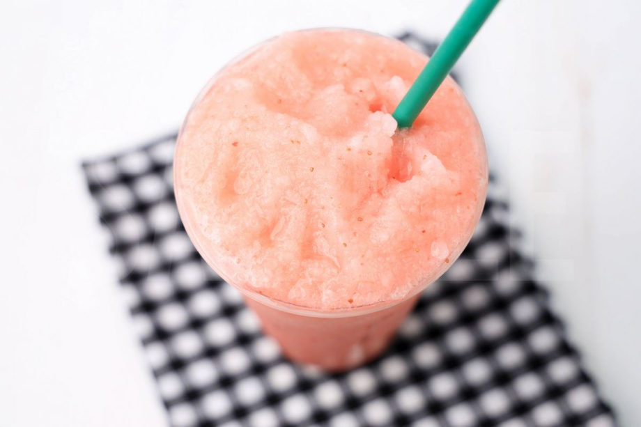 The Blended Strawberry Lemonade comes in a venti cup with a plaid napkin on a white wood backdrop.