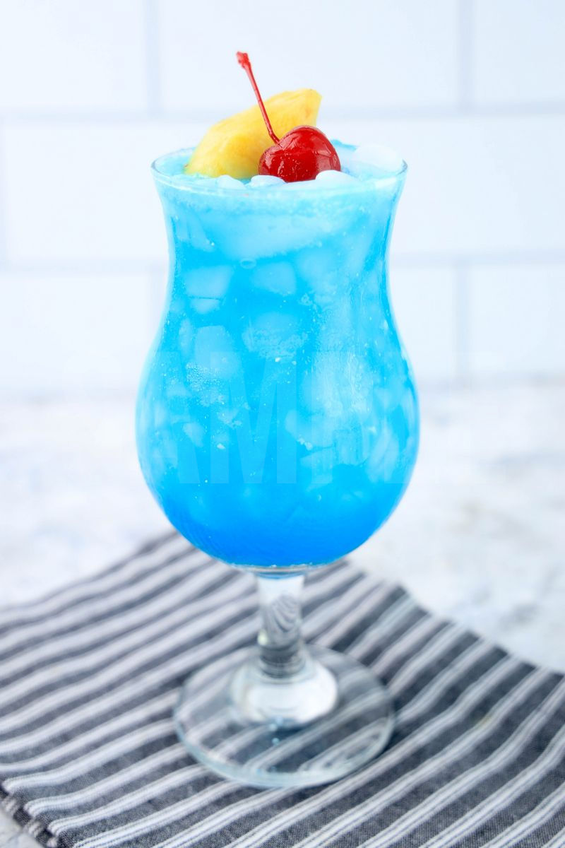 The Blue Hawaii Cocktail comes in a hurricane glass with a gray striped napkin on a marble backdrop.