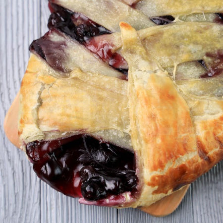 The Blueberry Puff Pastry Braid comes on a olive wood board on a gray wood backdrop.