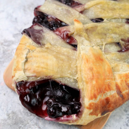 The Blueberry Puff Pastry Braid comes on a olive wood board on a marble backdrop.