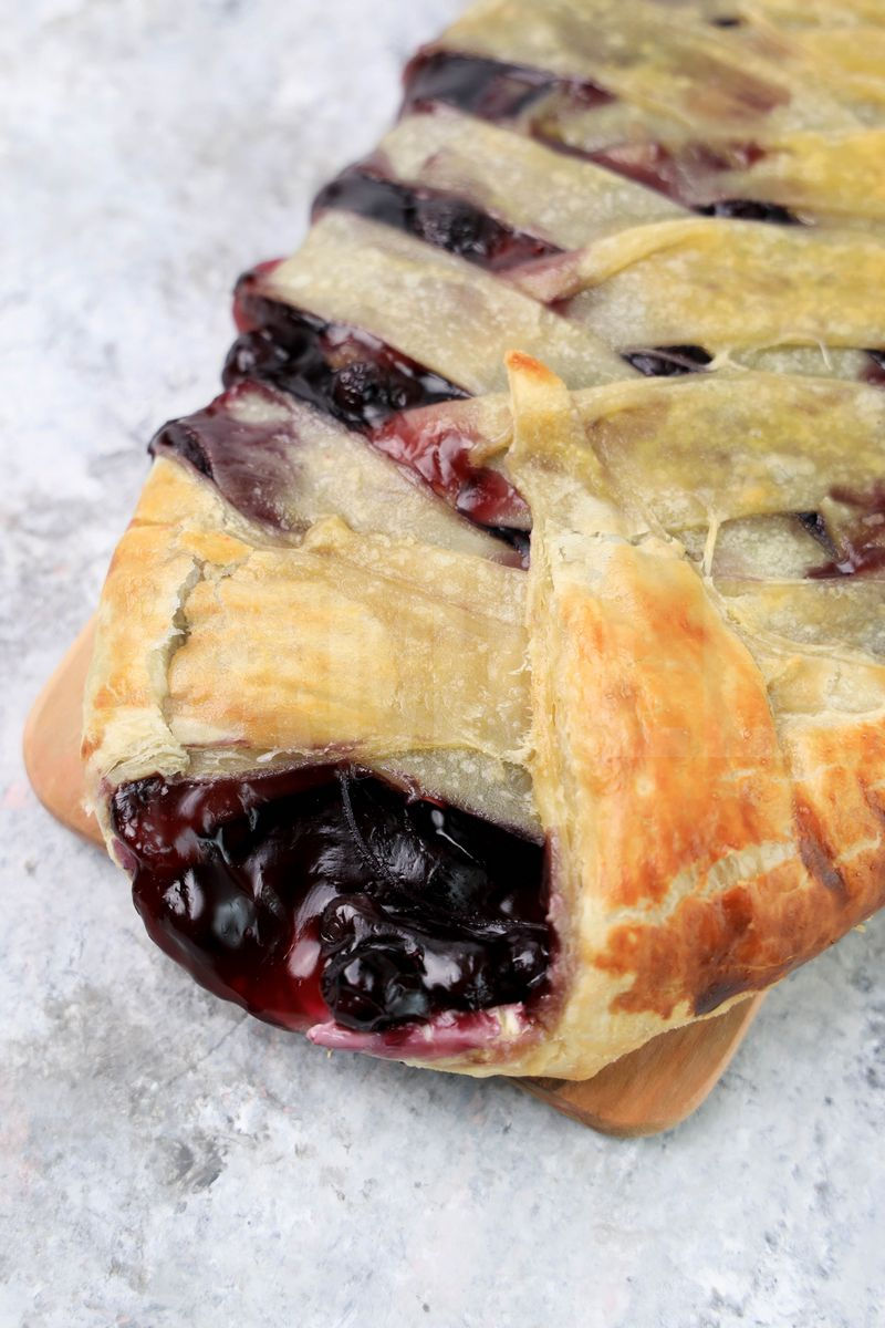 The Blueberry Puff Pastry Braid comes on a olive wood board on a marble backdrop.