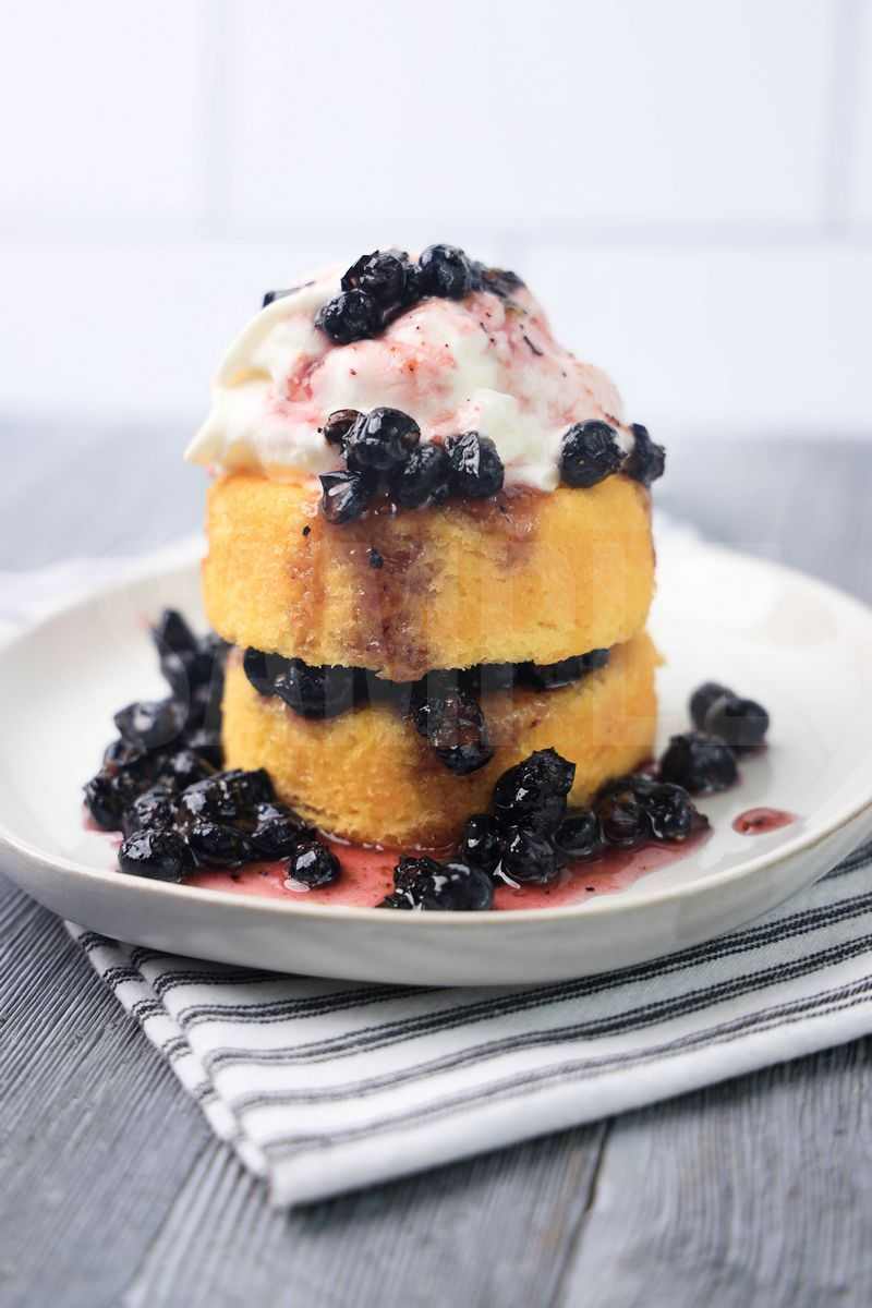 The Blueberry Shortcake comes on a white plate with a white striped napkin on a gray wood backdrop.