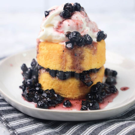 The Blueberry Shortcake comes on a white plate with a gray striped napkin on a marble backdrop.