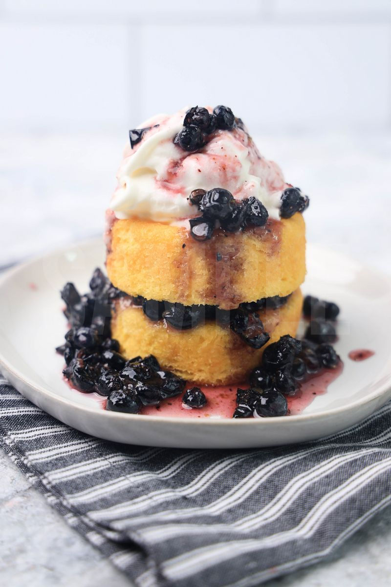 The Blueberry Shortcake comes on a white plate with a gray striped napkin on a marble backdrop.