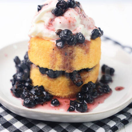 The Blueberry Shortcake comes on a white plate with a plaid napkin on a white wood backdrop.